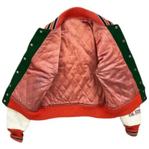 An open view of an orange varsity jacket showcasing a dusty pink diamond-quilted lining, contrasting with the rugged biker-style exterior patches.