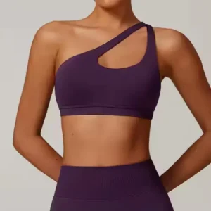 A woman wearing a plum purple one-shoulder sports bra with a matching diagonal cut-out design, paired with high-waisted leggings.